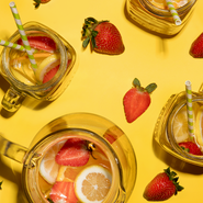 Zwei Gläser mit buntem Getränk, gefüllt mit Erdbeeren und Zitronenscheiben, stehen auf einer leuchtend gelben Oberfläche.