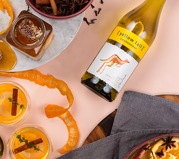 Ein Flasche Yellow Tail Chardonnay steht neben Gläsern mit orangefarbenen Cocktails und Gewürzen auf einem eleganten Tisch.