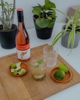 Eine Flasche Roséwein steht neben einem Glas mit einem erfrischenden Cocktail, garniert mit frischer Minze.