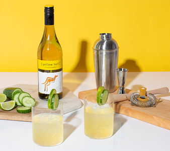 Eine Flasche Yellow Tail Chardonnay und ein Cocktailshaker sind neben zwei Gläsern mit einem spritzigen Getränk platziert.