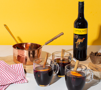 Ein kupferner Topf steht neben drei Gläsern mit heißem Getränk, dekoriert mit Zimtstangen und einer Flasche Rotwein.
