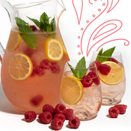 Ein Krug mit erfrischendem Getränk, gefüllt mit Zitronenscheiben, Himbeeren und frischer Minze, steht neben zwei Gläsern.