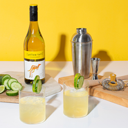 Eine Flasche Yellow Tail Chardonnay und ein Cocktailshaker sind neben zwei Gläsern mit einem spritzigen Getränk platziert.