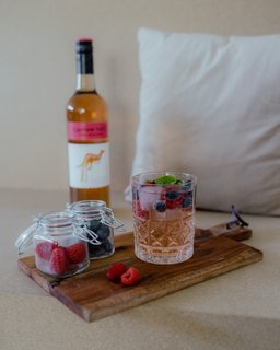 Ein elegantes Glas mit einem fruchtigen Getränk, gefüllt mit Himbeeren und Blaubeeren, steht auf einem Holzbrett.