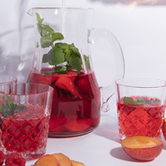 Ein Krug mit fruchtigem Getränk, gefüllt mit frischen Äpfeln und Minze, steht neben zwei Gläsern auf einem weißen Tisch.
