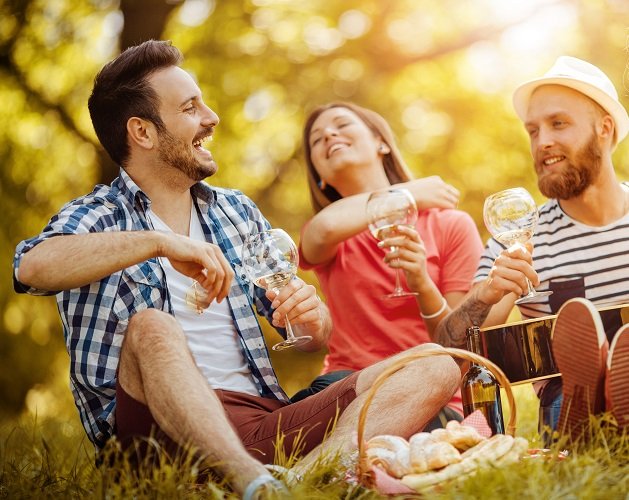 Drei Freunde genießen einen entspannten Nachmittag im Freien, während sie mit Gläsern anstoßen und lachen.