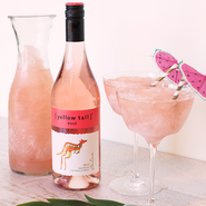 Eine Flasche Roséwein mit dem Etikett '[yellow tail]' steht neben einem Krug und zwei Gläsern mit gefrorenem Getränk.