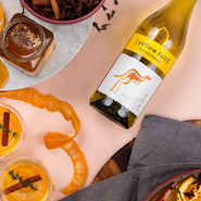 Ein Flasche Yellow Tail Chardonnay steht neben Gläsern mit orangefarbenen Cocktails und Gewürzen auf einem eleganten Tisch.