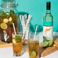 Ein großer Glasbehälter mit erfrischendem Getränk, Limetten und Minze, umgeben von zwei Gläsern und einer Flasche Wein.