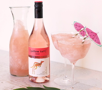 Eine Flasche Roséwein mit dem Etikett '[yellow tail]' steht neben einem Krug und zwei Gläsern mit gefrorenem Getränk.