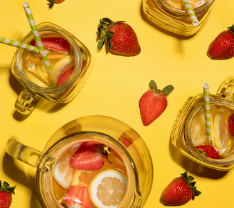 Zwei Gläser mit buntem Getränk, gefüllt mit Erdbeeren und Zitronenscheiben, stehen auf einer leuchtend gelben Oberfläche.